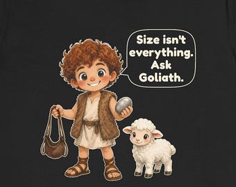 May include: A black t-shirt featuring a cartoon illustration of a curly-haired person in a fur vest holding a sling and a stone, standing next to a white lamb. A speech bubble contains the text: Size isn't everything. Ask Goliath.