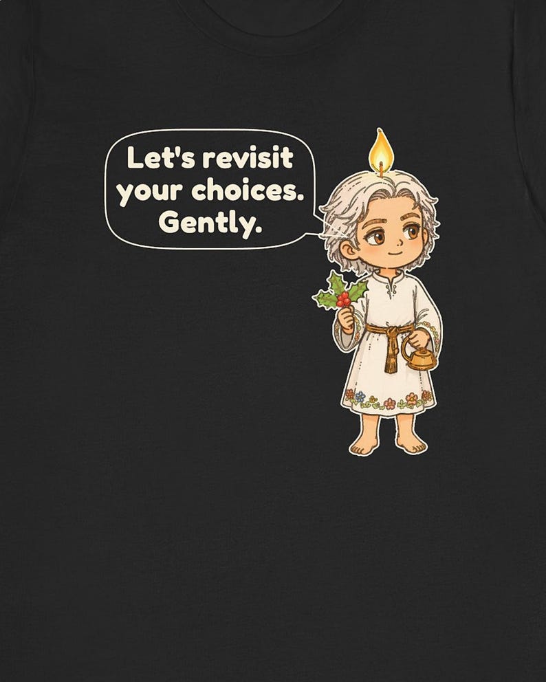 May include: A black t-shirt featuring a cartoon character with a candle flame on their head, holding a sprig of holly and a small gold kettle. A speech bubble contains the text: Let's revisit your choices. Gently. The character wears a white tunic.