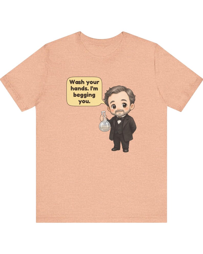 May include: A peach-colored t-shirt featuring a cartoon illustration of a man in a black suit and bowtie holding a glass flask. A speech bubble next to him contains the text: Wash your hands. I'm begging you.