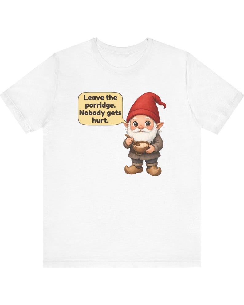 May include: A white t-shirt featuring a graphic of a gnome wearing a red hat and brown clothing, holding a wooden bowl and spoon. A speech bubble next to the gnome contains the text: Leave the porridge. Nobody gets hurt.