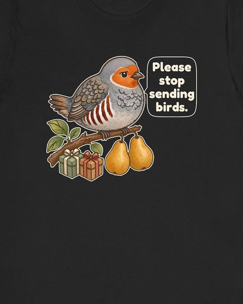 K&ouml;nnte beinhalten: Ein schwarzes T-Shirt mit einer Grafik eines grauen und orangefarbenen Vogels, der auf einem Ast mit zwei gelben Birnen und zwei kleinen Geschenkkartons sitzt. Eine Sprechblase neben dem Vogel enth&auml;lt den wei&szlig;en Text: Please stop sending birds.