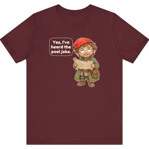 May include: A maroon t-shirt featuring a cartoon illustration of a bearded character wearing a red cap and green coat, holding a map. A speech bubble above the character contains the text, "Yes, I've heard the pool joke."
