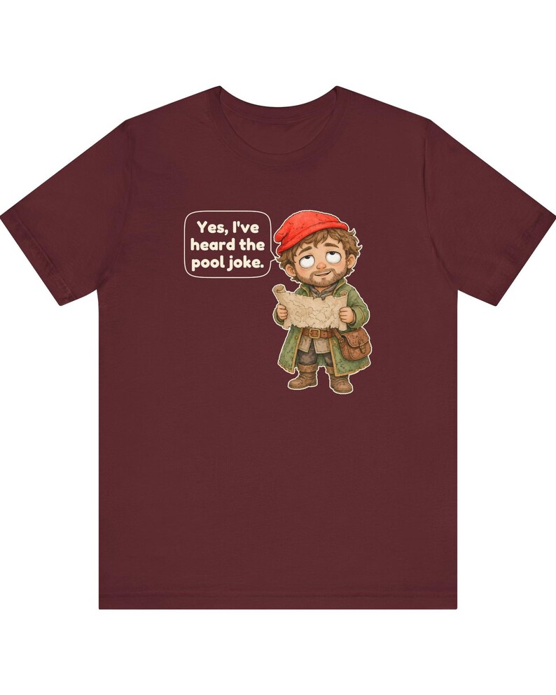 May include: A maroon t-shirt featuring a cartoon illustration of a bearded character wearing a red cap and green coat, holding a map. A speech bubble above the character contains the text, "Yes, I've heard the pool joke."