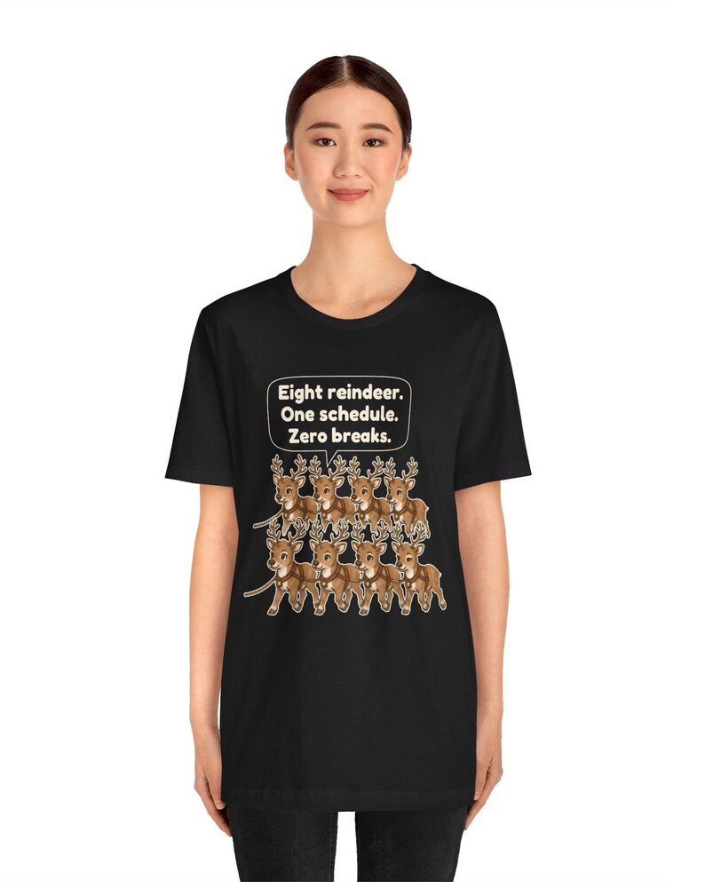 K&ouml;nnte beinhalten: Ein schwarzes Kurzarm-T-Shirt mit einer Grafik von acht braunen Rentieren, die in zwei Reihen angeordnet sind. &Uuml;ber den Rentieren befindet sich eine wei&szlig;e Sprechblase mit dem Text: Eight reindeer. One schedule. Zero breaks.