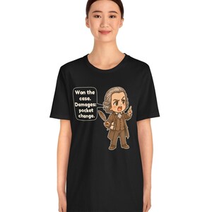 May include: A black t-shirt featuring a cartoon illustration of a historical figure in a brown suit holding a quill. A speech bubble next to the character contains the text: Won the case. Damages: pocket change. The design is centered on the chest.