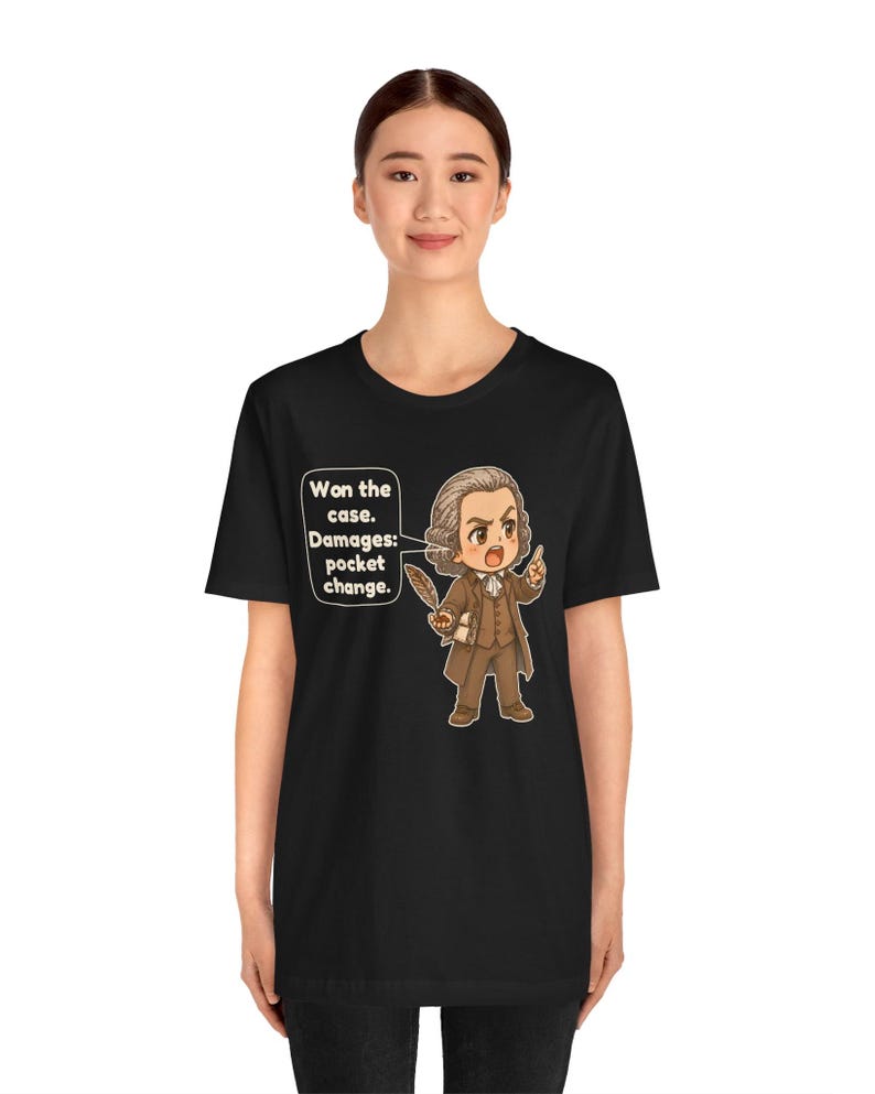 May include: A black t-shirt featuring a cartoon illustration of a historical figure in a brown suit holding a quill. A speech bubble next to the character contains the text: Won the case. Damages: pocket change. The design is centered on the chest.