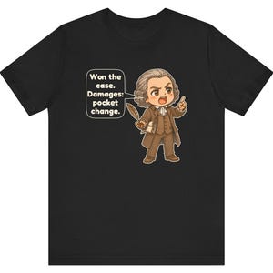 May include: A black t-shirt featuring a cartoon illustration of a historical figure in a brown suit holding a quill. A speech bubble contains the text: Won the case. Damages: pocket change. The character has a powdered wig and an expressive face.