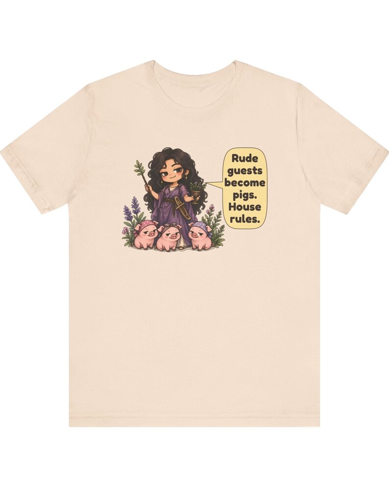 May include: A light beige t-shirt featuring a graphic of a dark-haired figure in a purple robe holding a staff and a cup, surrounded by three small pigs. A speech bubble contains the text: Rude guests become pigs. House rules.