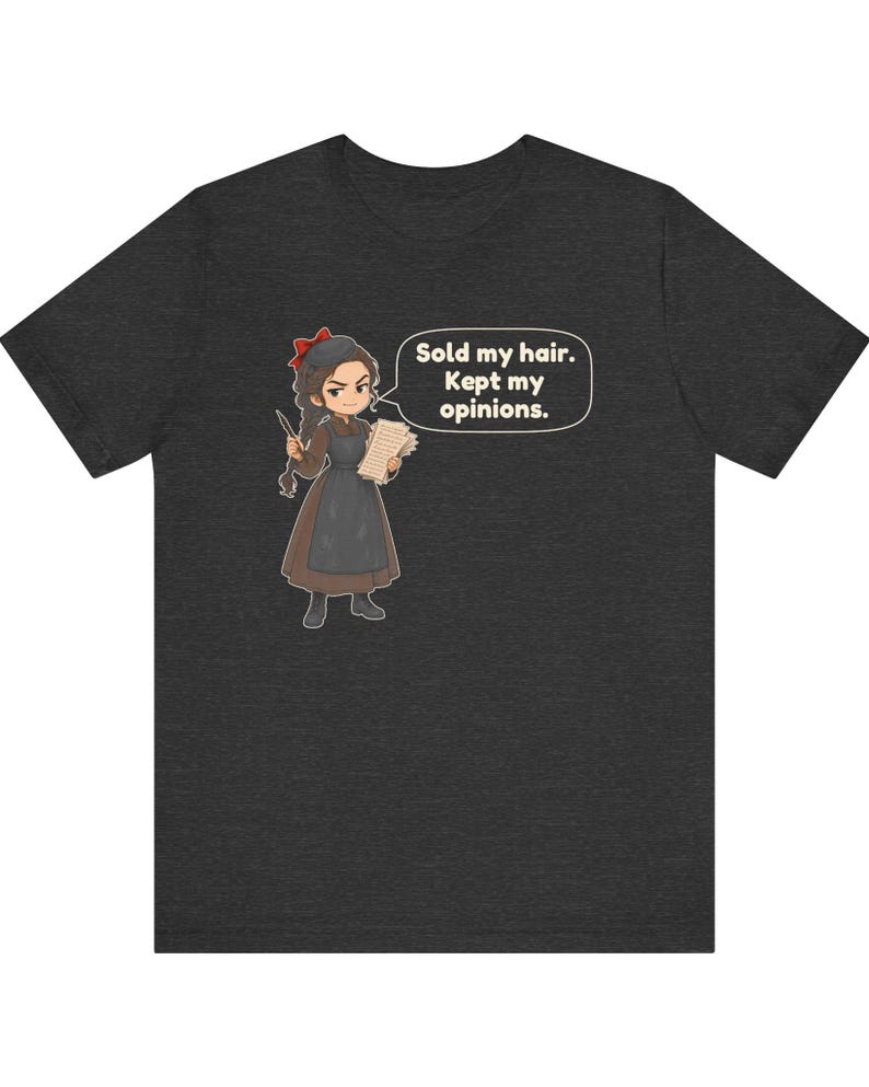 May include: A dark heather gray t-shirt featuring a cartoon illustration of a person with braided hair wearing a brown dress and black apron. The character holds a quill and paper, with a speech bubble containing the text: Sold my hair. Kept my opinions.