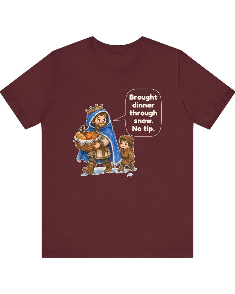 May include: A maroon t-shirt featuring a graphic of a king in a blue cape carrying a basket of bread with a child, accompanied by a speech bubble that reads: Brought dinner through snow. No tip.
