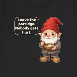 May include: A black t-shirt featuring a cartoon gnome wearing a red hat and brown clothing, holding a wooden bowl of porridge with a spoon. A speech bubble contains the text: Leave the porridge. Nobody gets hurt. The gnome has a white beard.