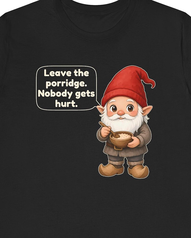 May include: A black t-shirt featuring a cartoon gnome wearing a red hat and brown clothing, holding a wooden bowl of porridge with a spoon. A speech bubble contains the text: Leave the porridge. Nobody gets hurt. The gnome has a white beard.