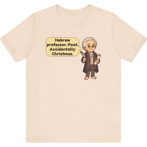 Pu&ograve; includere: Una t-shirt beige chiaro con un'illustrazione a cartone animato di una persona con capelli grigi, occhiali e un cappotto scuro che tiene in mano una penna e una pergamena. Un fumetto giallo contiene il testo: Hebrew professor. Poet. Accidentally Christmas.