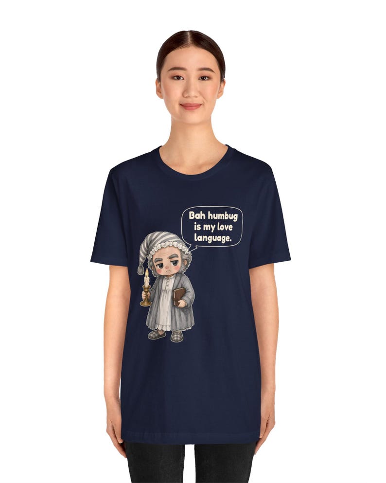 Puede incluir: Una camiseta azul marino de manga corta con el gr&aacute;fico de un personaje con gorro de dormir y bata que sostiene una vela y un libro. Un globo de texto sobre el personaje contiene el texto: "Bah humbug is my love language."
