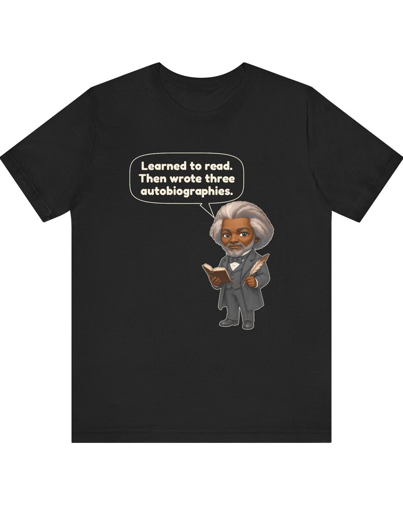 Puede incluir: Una camiseta negra con una ilustraci&oacute;n de estilo caricatura de Frederick Douglass sosteniendo un libro y una pluma. Un globo de texto sobre la figura contiene el texto: Learned to read. Then wrote three autobiographies.