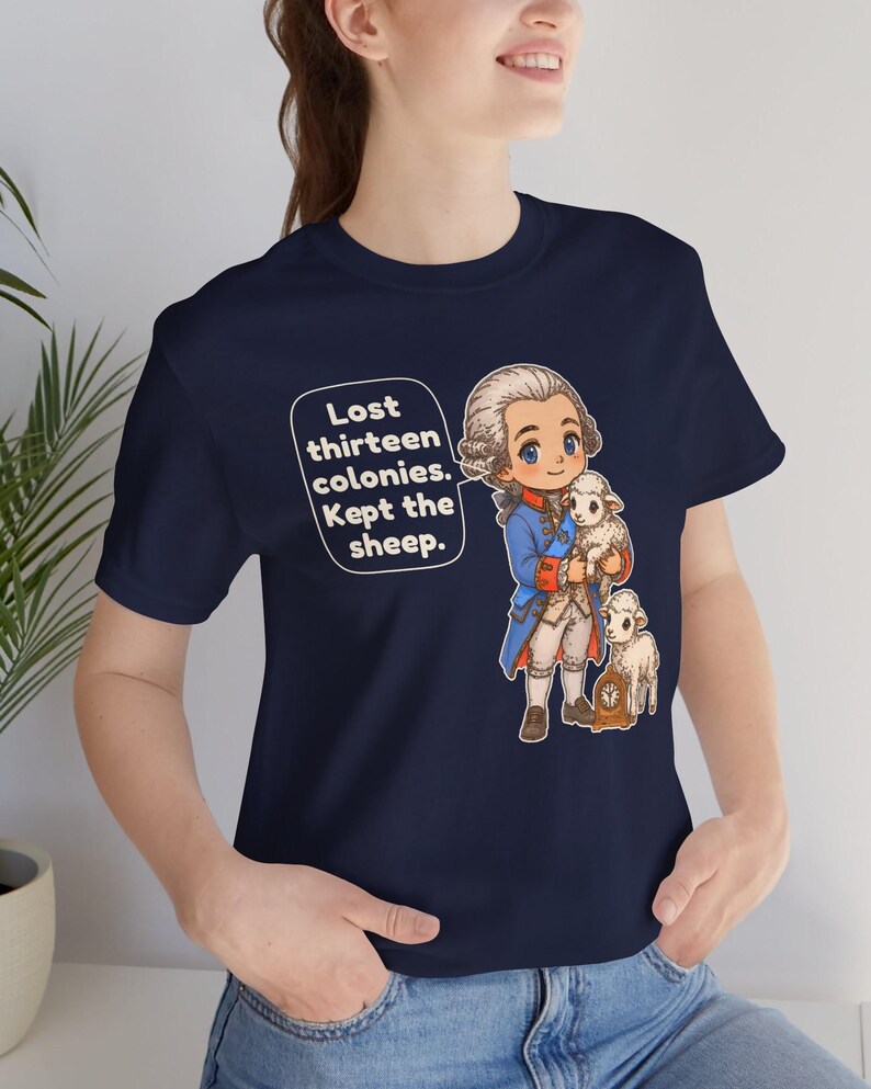 Peut inclure: Un t-shirt bleu marine avec une illustration de style dessin anim&eacute; repr&eacute;sentant un personnage historique en manteau bleu tenant un petit mouton, avec un autre mouton &agrave; c&ocirc;t&eacute; d'une horloge. La bulle contient le texte : Lost thirteen colonies. Kept the sheep.