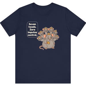 May include: A navy blue short-sleeve t-shirt featuring a graphic of a seven-headed mouse wearing small gold crowns and holding a piece of yellow cheese. The text "Seven heads. Zero impulse control." is printed in white next to the mouse.