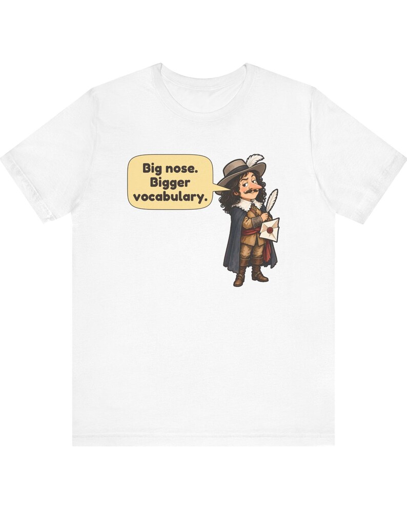 May include: A white t-shirt featuring a cartoon illustration of a historical figure with a large nose, wearing a hat with a feather, a cape, and holding a quill and letter. A speech bubble contains the text: Big nose. Bigger vocabulary.