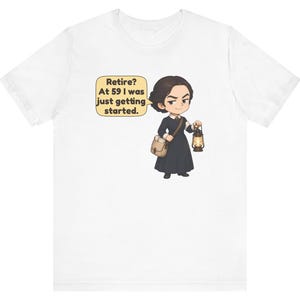 May include: A white t-shirt featuring a cartoon illustration of a person with dark hair wearing a long black dress, carrying a tan satchel and a lit lantern. A yellow speech bubble contains the text: Retire? At 59 I was just getting started.