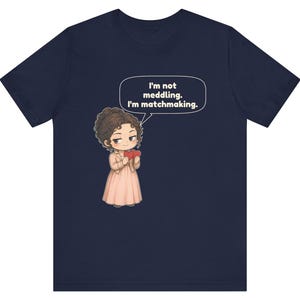 K&ouml;nnte beinhalten: Ein marineblaues Kurzarm-T-Shirt mit einer Cartoon-Illustration einer Person mit braunen Haaren in einem hellrosa Kleid, die zwei rote Herzen h&auml;lt. Eine Sprechblase &uuml;ber der Figur enth&auml;lt den Text: I'm not meddling. I'm matchmaking.
