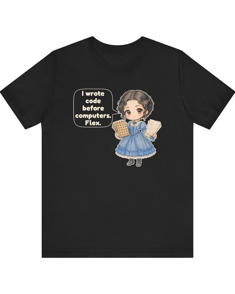 May include: A black t-shirt featuring a cartoon illustration of a person in a blue Victorian-style dress holding punch cards and papers. A speech bubble next to the character contains the text: I wrote code before computers. Flex.