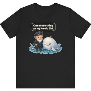 May include: A black t-shirt featuring a graphic of a sea captain with a white beard and a white whale in blue ocean waves. Above the captain is a speech bubble with the text, One more thing on my to-do list. The design is centered on the chest.