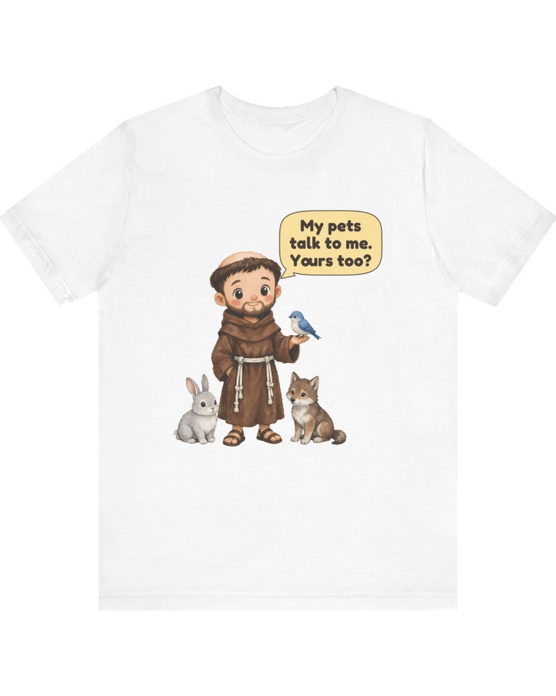 May include: A white t-shirt featuring a cartoon illustration of a monk in a brown robe standing with a grey rabbit, a brown wolf, and a blue bird. A speech bubble above the monk contains the text: My pets talk to me. Yours too?