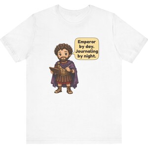 K&ouml;nnte beinhalten: Ein wei&szlig;es T-Shirt mit einer Cartoon-Illustration eines b&auml;rtigen Kaisers in r&ouml;mischer R&uuml;stung und violettem Umhang, der ein Tagebuch und einen Stift h&auml;lt. Eine Sprechblase enth&auml;lt den Text: Emperor by day. Journaling by night.