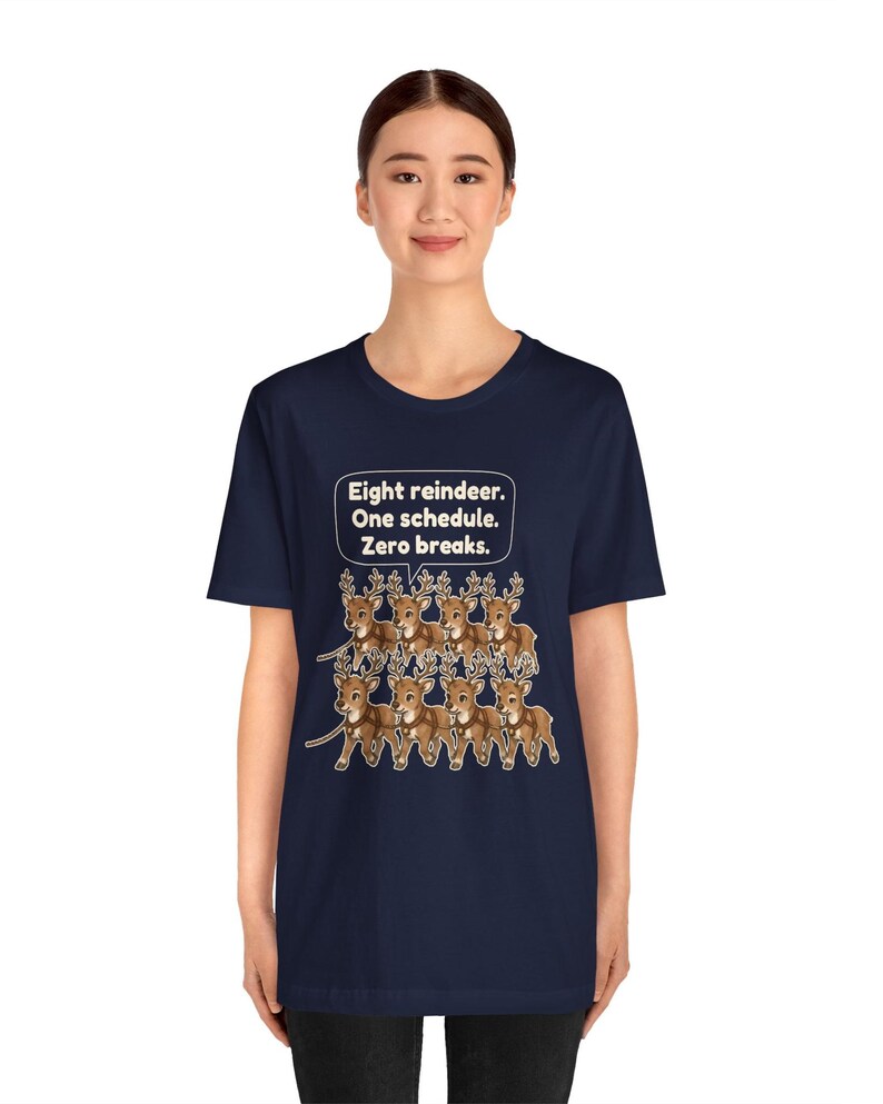 K&ouml;nnte beinhalten: Ein dunkelblaues Kurzarm-T-Shirt mit einer Grafik von acht braunen Rentieren in zwei Reihen. &Uuml;ber den Rentieren befindet sich eine Sprechblase mit dem wei&szlig;en Text: Eight reindeer. One schedule. Zero breaks.