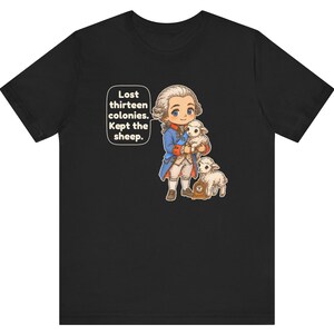Peut inclure: Un t-shirt noir avec une illustration de style dessin anim&eacute; repr&eacute;sentant un personnage historique en manteau bleu et perruque blanche tenant un agneau, avec un autre agneau et une horloge. Une bulle contient le texte : Lost thirteen colonies. Kept the sheep.