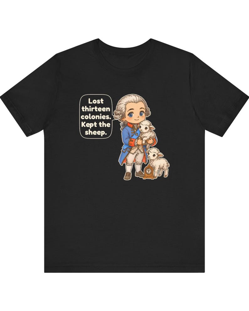 Peut inclure: Un t-shirt noir avec une illustration de style dessin anim&eacute; repr&eacute;sentant un personnage historique en manteau bleu et perruque blanche tenant un agneau, avec un autre agneau et une horloge. Une bulle contient le texte : Lost thirteen colonies. Kept the sheep.