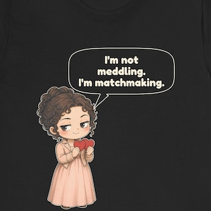 K&ouml;nnte beinhalten: Ein schwarzes T-Shirt mit einer Cartoon-Illustration einer Person mit lockigem braunem Haar, die ein hellrosa Kleid und eine Jacke tr&auml;gt. Die Figur h&auml;lt zwei rote Herzen und eine Sprechblase mit dem Text, I'm not meddling. I'm matchmaking.