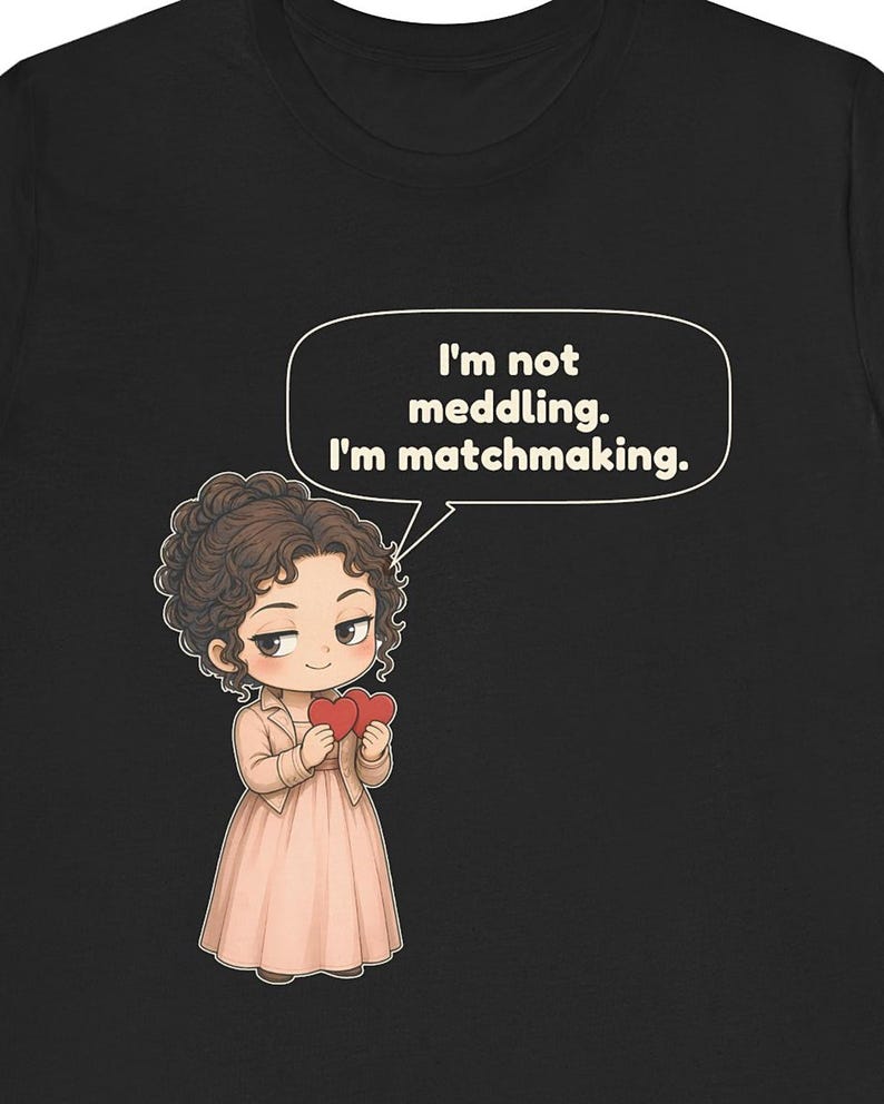 K&ouml;nnte beinhalten: Ein schwarzes T-Shirt mit einer Cartoon-Illustration einer Person mit lockigem braunem Haar, die ein hellrosa Kleid und eine Jacke tr&auml;gt. Die Figur h&auml;lt zwei rote Herzen und eine Sprechblase mit dem Text, I'm not meddling. I'm matchmaking.