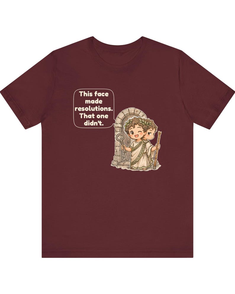 K&ouml;nnte beinhalten: Ein kastanienbraunes T-Shirt mit einer Grafik einer zweigesichtigen Figur, die einen Lorbeerkranz und eine Toga tr&auml;gt und vor einem Steinbogen steht. Die Figur h&auml;lt einen Schl&uuml;ssel und einen Stab. Eine Sprechblase enth&auml;lt den Text: This face made resolutions. That one didn't.