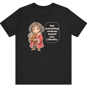 May include: A black t-shirt featuring a cartoon illustration of a person in a red coat holding a golden armillary sphere. A speech bubble next to the figure contains the text: Not everything revolves around you. Literally.