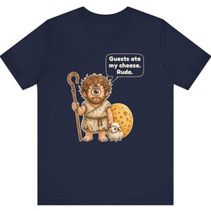 May include: A navy blue t-shirt featuring a graphic of a one-eyed cyclops holding a wooden staff and standing next to a large wheel of cheese and a small sheep. A speech bubble above the cyclops contains the text: Guests ate my cheese. Rude.