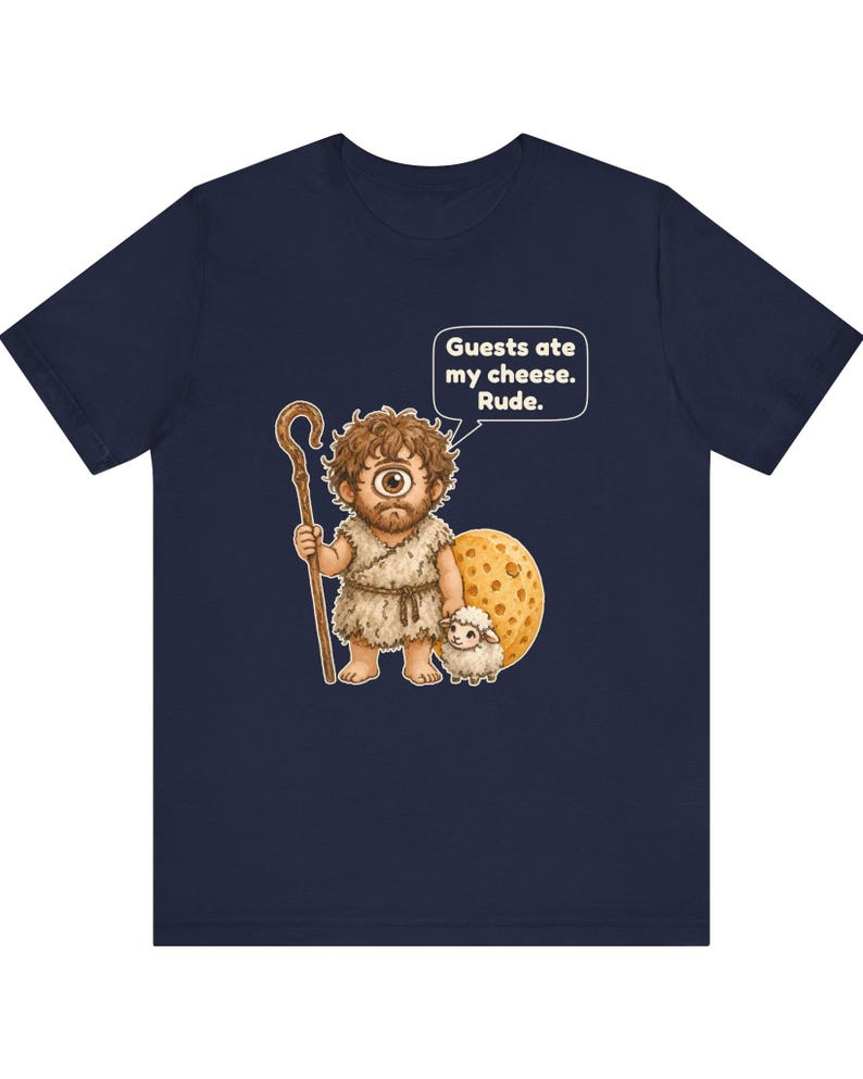 May include: A navy blue t-shirt featuring a graphic of a one-eyed cyclops holding a wooden staff and standing next to a large wheel of cheese and a small sheep. A speech bubble above the cyclops contains the text: Guests ate my cheese. Rude.