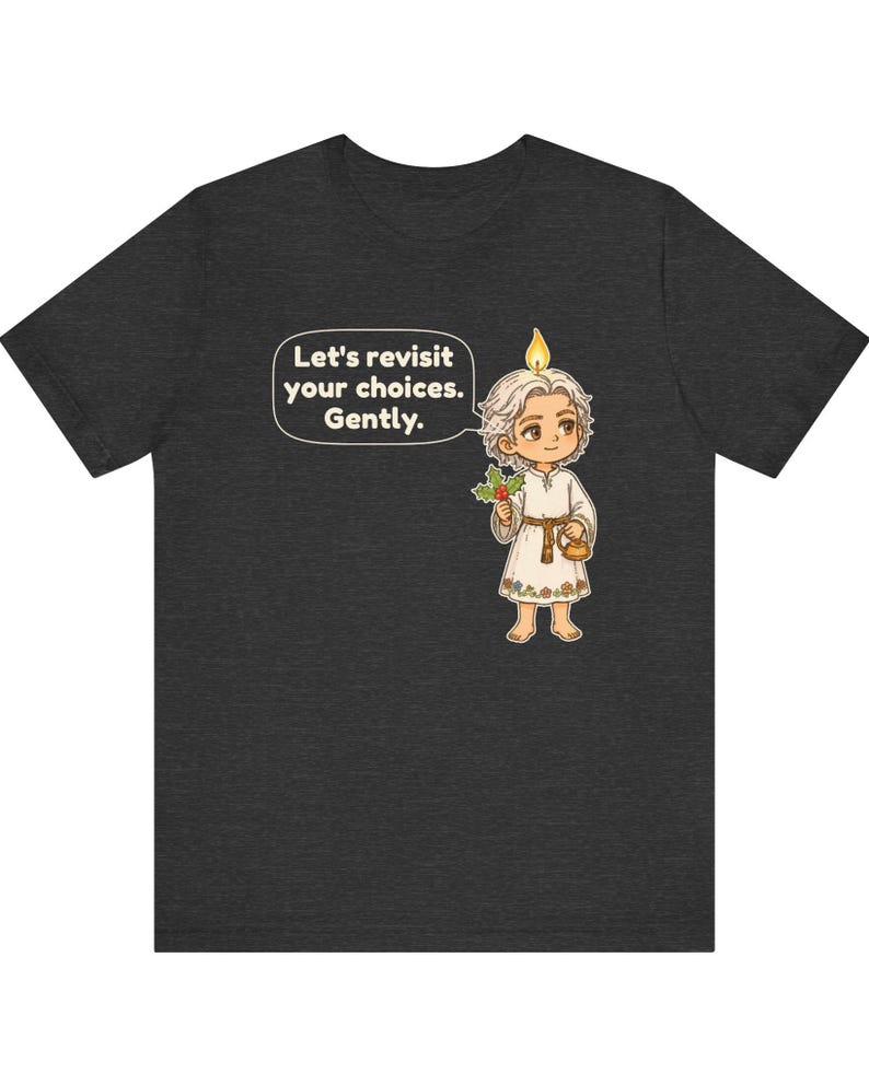 May include: A dark gray t-shirt featuring a cartoon character with a candle flame on their head, holding a sprig of holly and a small teapot. A speech bubble contains the text: Let's revisit your choices. Gently. The character wears a white tunic.
