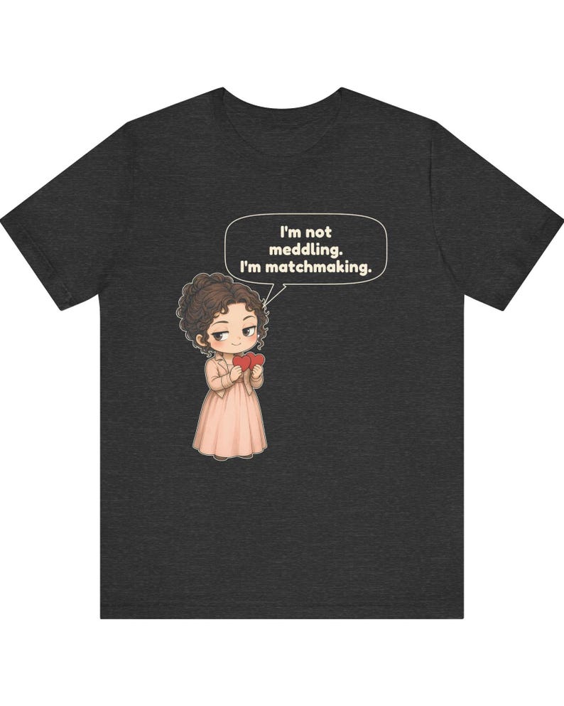 K&ouml;nnte beinhalten: Ein dunkelgraues T-Shirt mit einer Cartoon-Illustration einer Person mit braunen Haaren in einem hellrosa Kleid, die zwei rote Herzen h&auml;lt. Eine Sprechblase &uuml;ber der Figur enth&auml;lt den Text: I'm not meddling. I'm matchmaking.