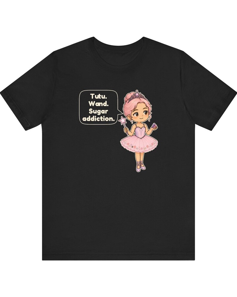 May include: A black t-shirt featuring a cartoon illustration of a ballerina with pink hair, a pink tutu, and a tiara. The character holds a star-tipped wand and a cupcake. A speech bubble contains the text: Tutu. Wand. Sugar addiction.