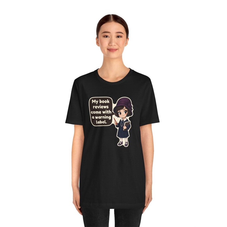K&ouml;nnte beinhalten: Ein schwarzes Kurzarm-T-Shirt mit einer Grafik einer Zeichentrickfigur, die einen dunklen Hut und ein Kleid tr&auml;gt und ein Buch h&auml;lt. Eine Sprechblase neben der Figur enth&auml;lt den Text: My book reviews come with a warning label.