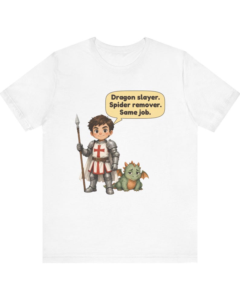 K&ouml;nnte beinhalten: Ein wei&szlig;es T-Shirt mit einer Grafik eines Cartoon-Ritters in silberner R&uuml;stung, der einen Speer h&auml;lt und neben einem kleinen gr&uuml;nen Drachen steht. Eine Sprechblase &uuml;ber dem Ritter enth&auml;lt den Text: Dragon slayer. Spider remover. Same job.