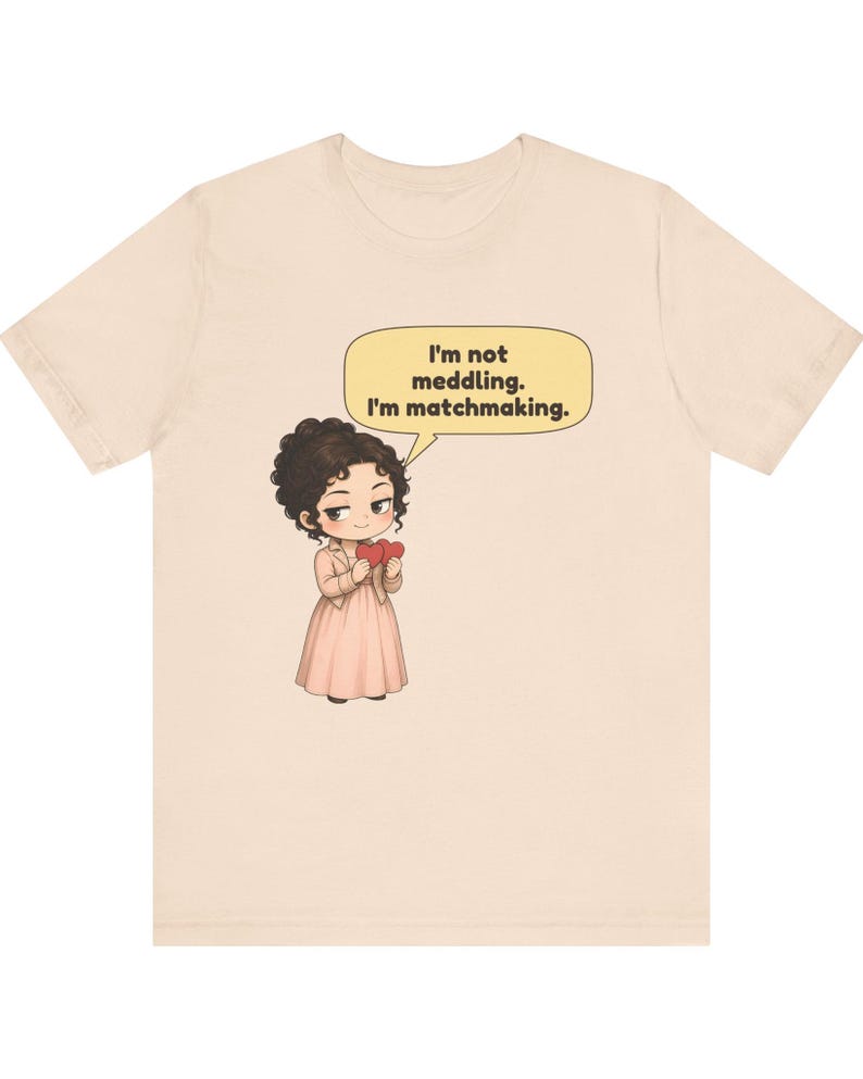 K&ouml;nnte beinhalten: Ein hellbeiges T-Shirt mit einer Cartoon-Illustration einer Person mit dunklen lockigen Haaren, die ein hellrosa Kleid und eine Jacke tr&auml;gt und zwei rote Herzen h&auml;lt. Eine gelbe Sprechblase dar&uuml;ber enth&auml;lt den Text: I'm not meddling. I'm matchmaking.