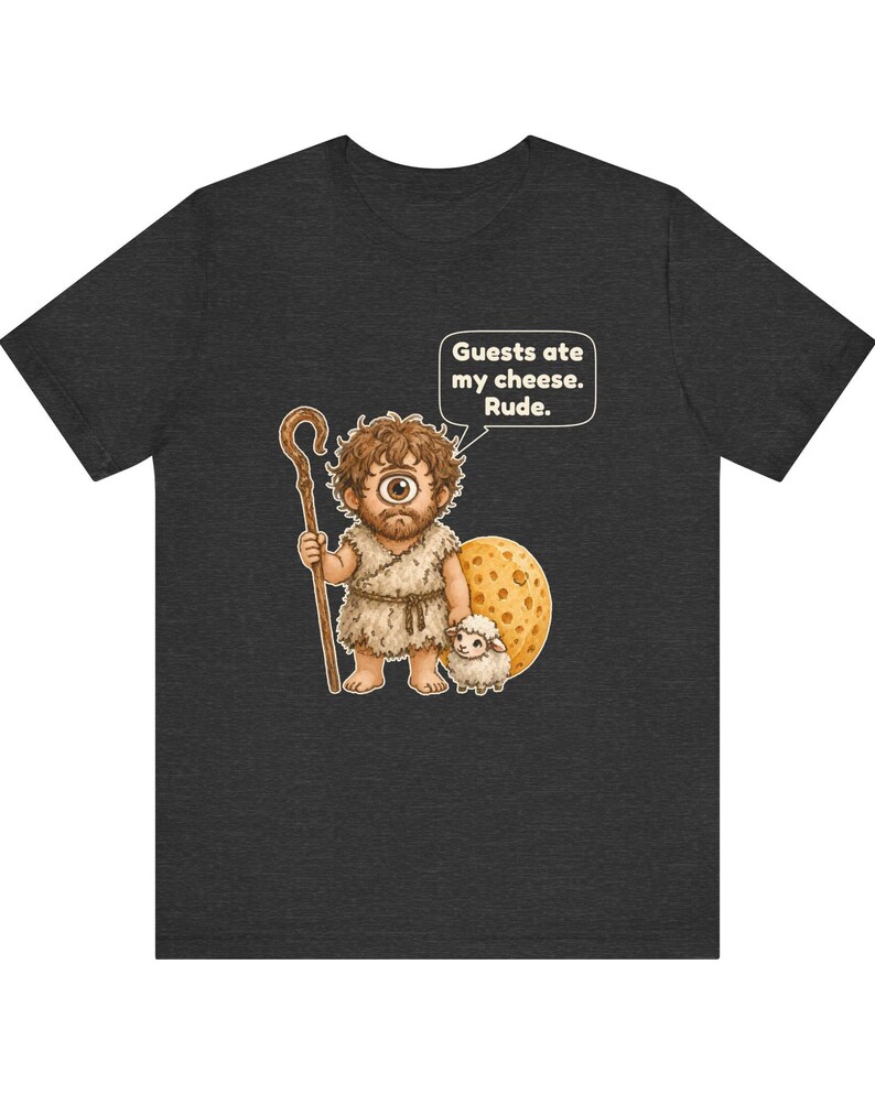May include: A dark gray t-shirt featuring a cartoon cyclops holding a wooden staff and standing next to a small sheep and a large piece of Swiss cheese. A speech bubble above the cyclops contains the text: Guests ate my cheese. Rude.