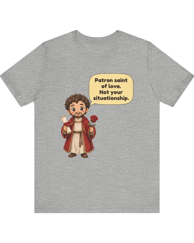 Puede incluir: Una camiseta gris jaspeado con una ilustraci&oacute;n de dibujos animados de una figura barbuda con t&uacute;nica roja que sostiene un pergamino y una rosa roja. Un globo de texto contiene: Patron saint of love. Not your situationship.