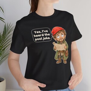 May include: A black t-shirt featuring a cartoon illustration of a bearded character wearing a red cap and green coat, holding a map. A speech bubble above the character contains the text, Yes, I've heard the pool joke.