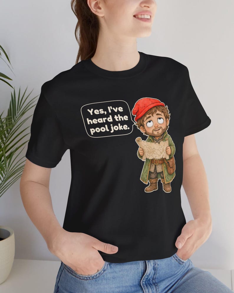May include: A black t-shirt featuring a cartoon illustration of a bearded character wearing a red cap and green coat, holding a map. A speech bubble above the character contains the text, Yes, I've heard the pool joke.