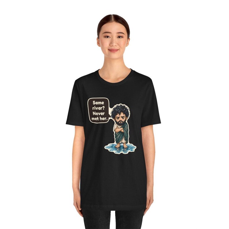 Może przedstawiać: Czarny t-shirt z rysunkową ilustracją brodatej osoby z kręconymi włosami stojącej w kałuży wody. Dymek obok postaci zawiera tekst: Same river? Never met her.
