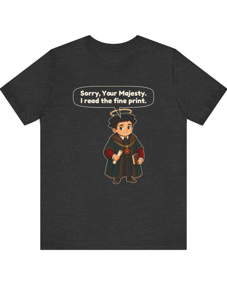 May include: A dark gray t-shirt featuring a cartoon character wearing a dark green robe, a gold chain, and a halo. The character holds a scroll and a book. A speech bubble above the character contains the text: Sorry, Your Majesty. I read the fine print.