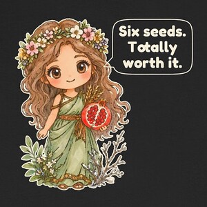 May include: A black t-shirt featuring a cartoon illustration of a girl with long brown hair wearing a flower crown and a green dress. She holds a pomegranate and wheat. A speech bubble contains the text: Six seeds. Totally worth it.